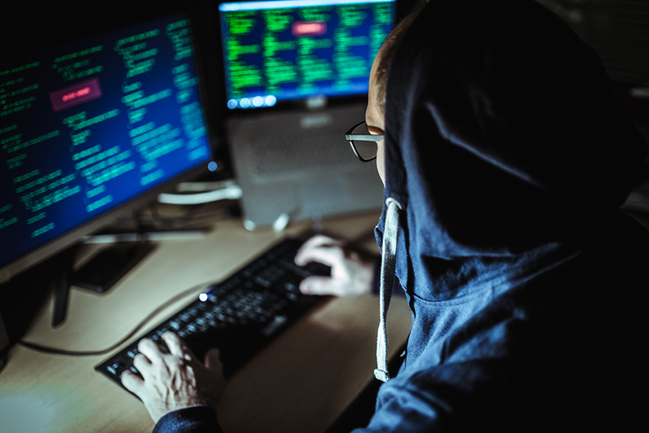 A hacker wearing a hoodie is decrypting intellectual property on their computer.