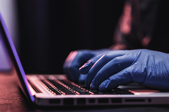 Two hands wearing gloves typing on a computer, committing an act of corporate espionage.