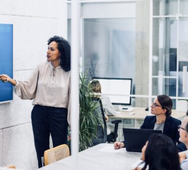 Businesswoman pointing at statistics on digital screen, giving presentation in conference room. Corporate coworkers listening to financial analytics report in office meeting