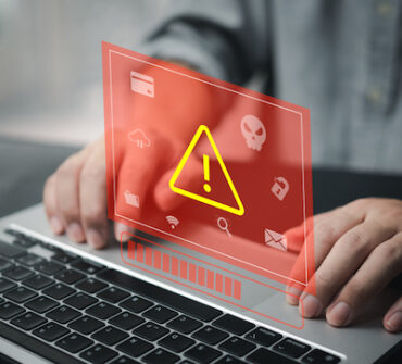 A malicious insider businessman using laptop computer with triangle caution warning sign.